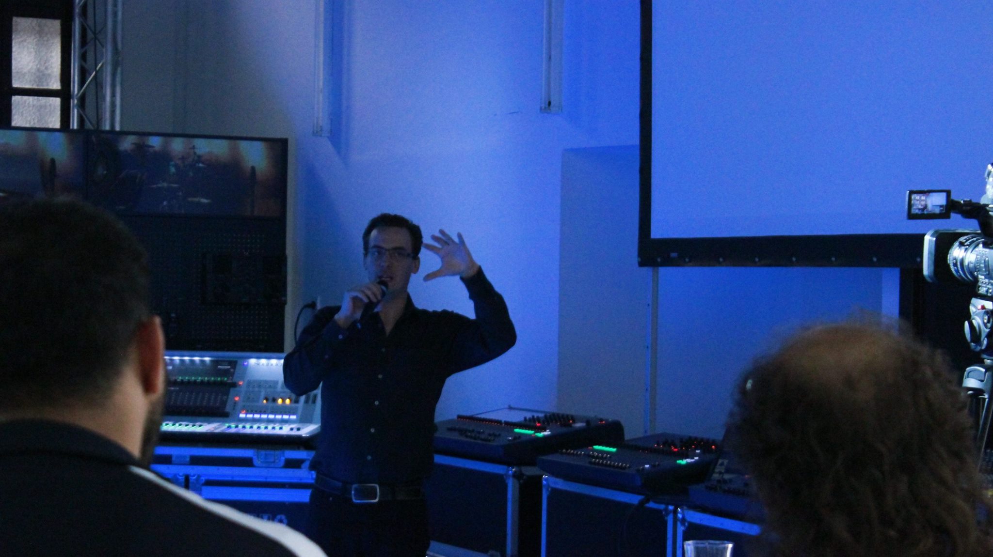 Sam speaking into a microphone in front of a group at a professional audio studio